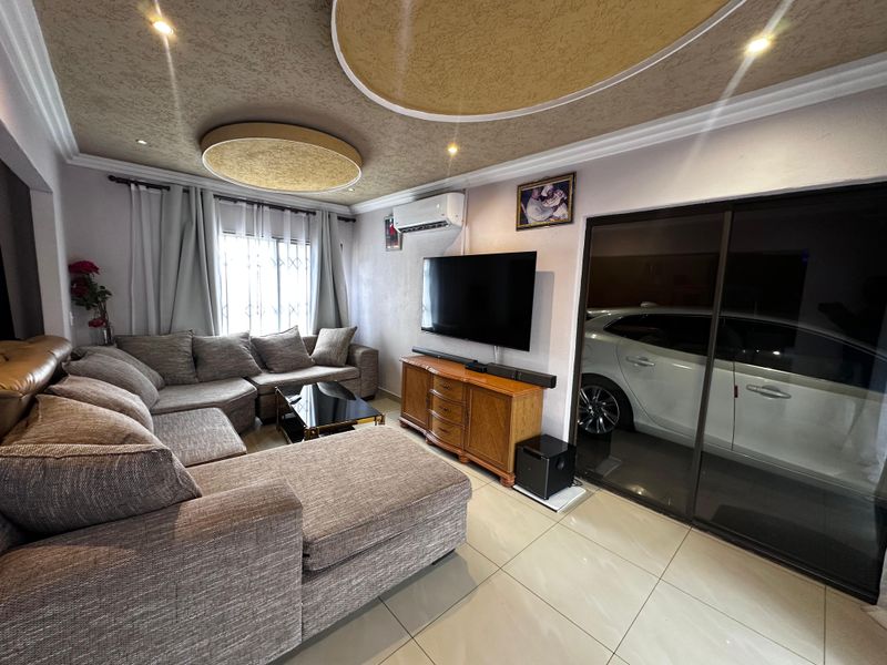 A comfortable living room featuring tiled flooring, a decorative recessed ceiling with circular accents, and a split-system air conditioner.