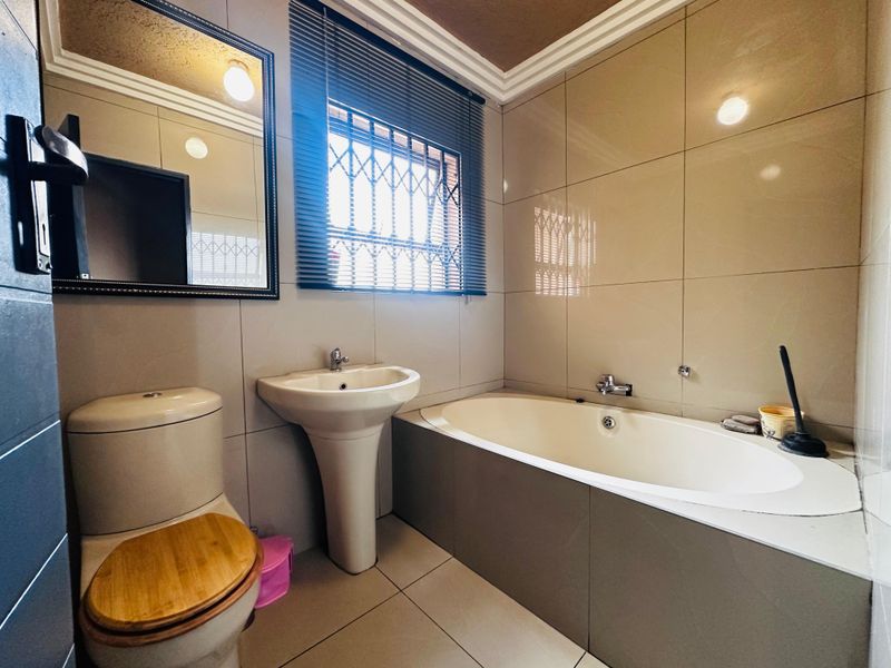 A well-maintained bathroom featuring a pedestal basin, built-in bathtub, toilet, and neutral wall tiling with secure window bars.