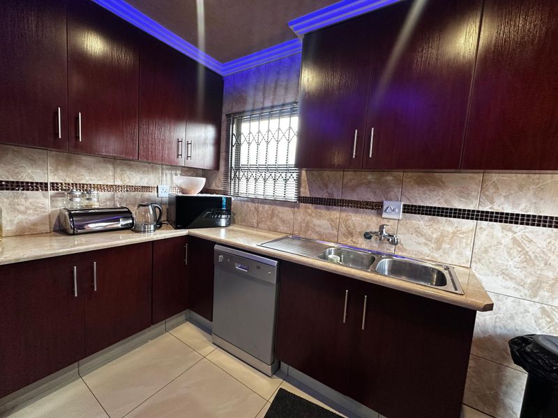 A functional kitchen featuring dark wood cabinetry, tiled backsplash, laminate countertops, and a double bowl stainless steel sink with integrated dishwasher.
