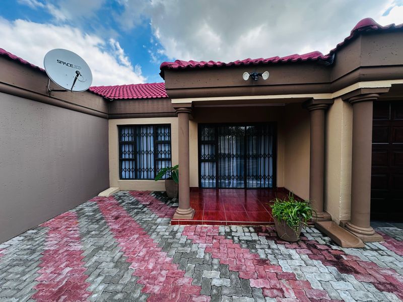 Front entrance of the house featuring a paved driveway, covered tiled patio, and security gates on windows and doors.