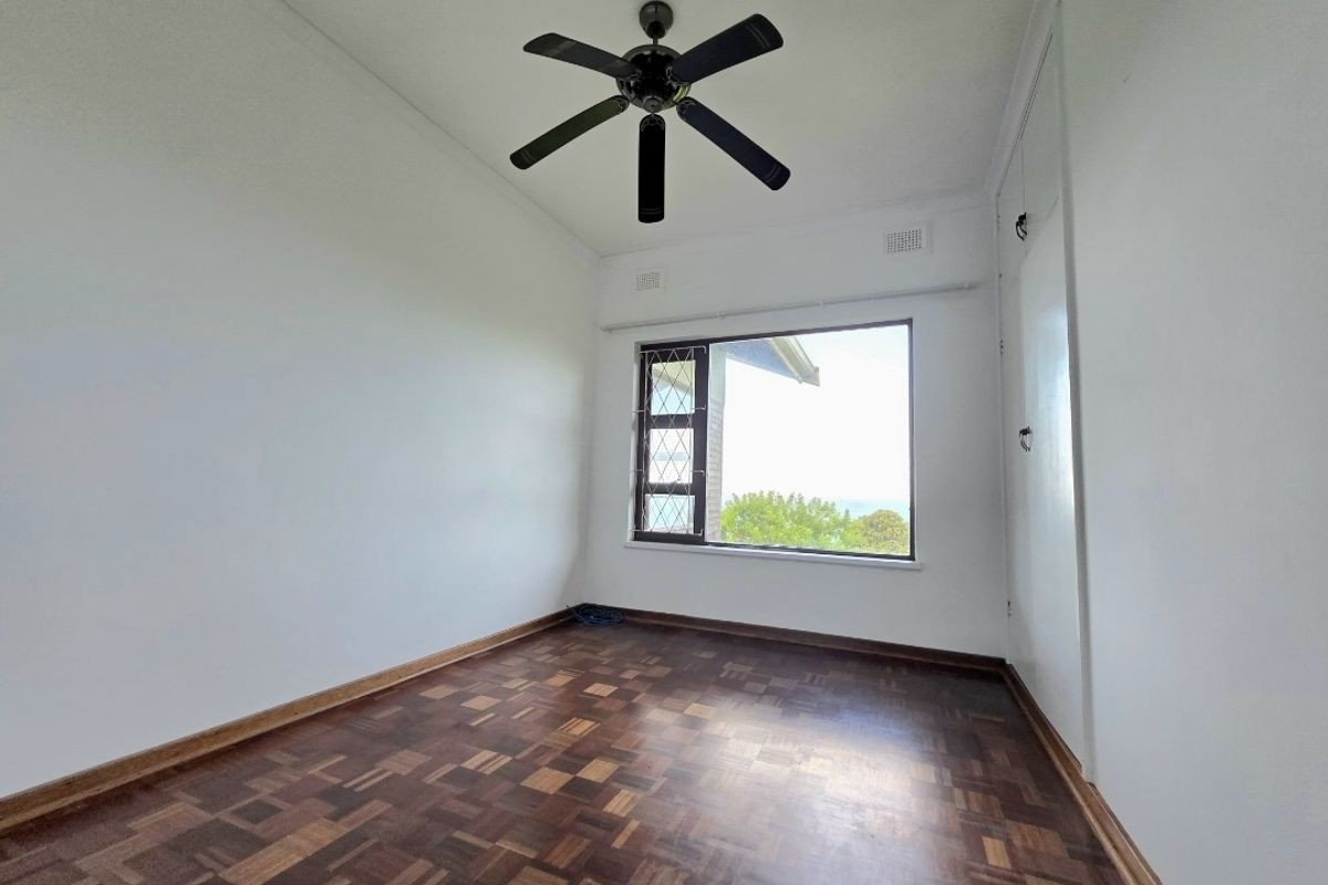 A bright, empty bedroom featuring classic parquet flooring, a ceiling fan, and a built-in cupboard, offering a clean canvas for personalization.