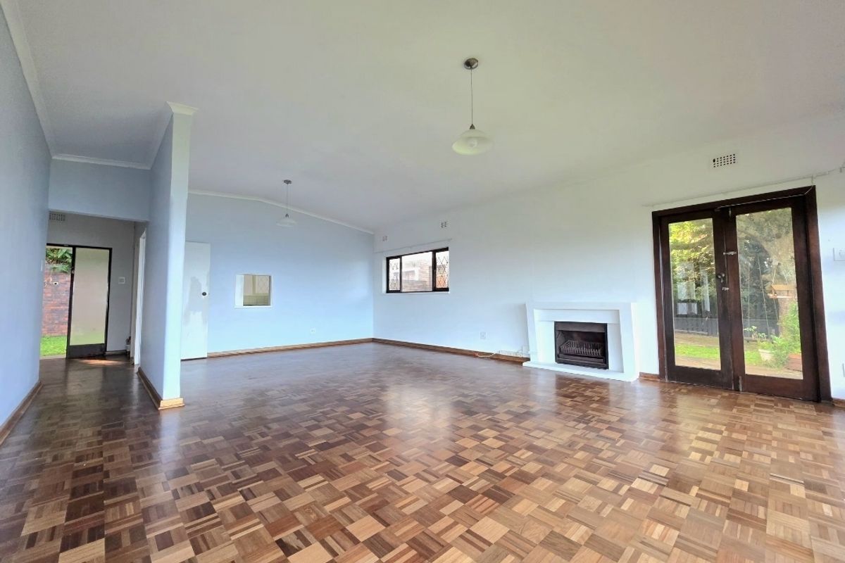 Spacious living room featuring classic parquet flooring, a built-in fireplace, and direct access to the garden through double glass doors.
