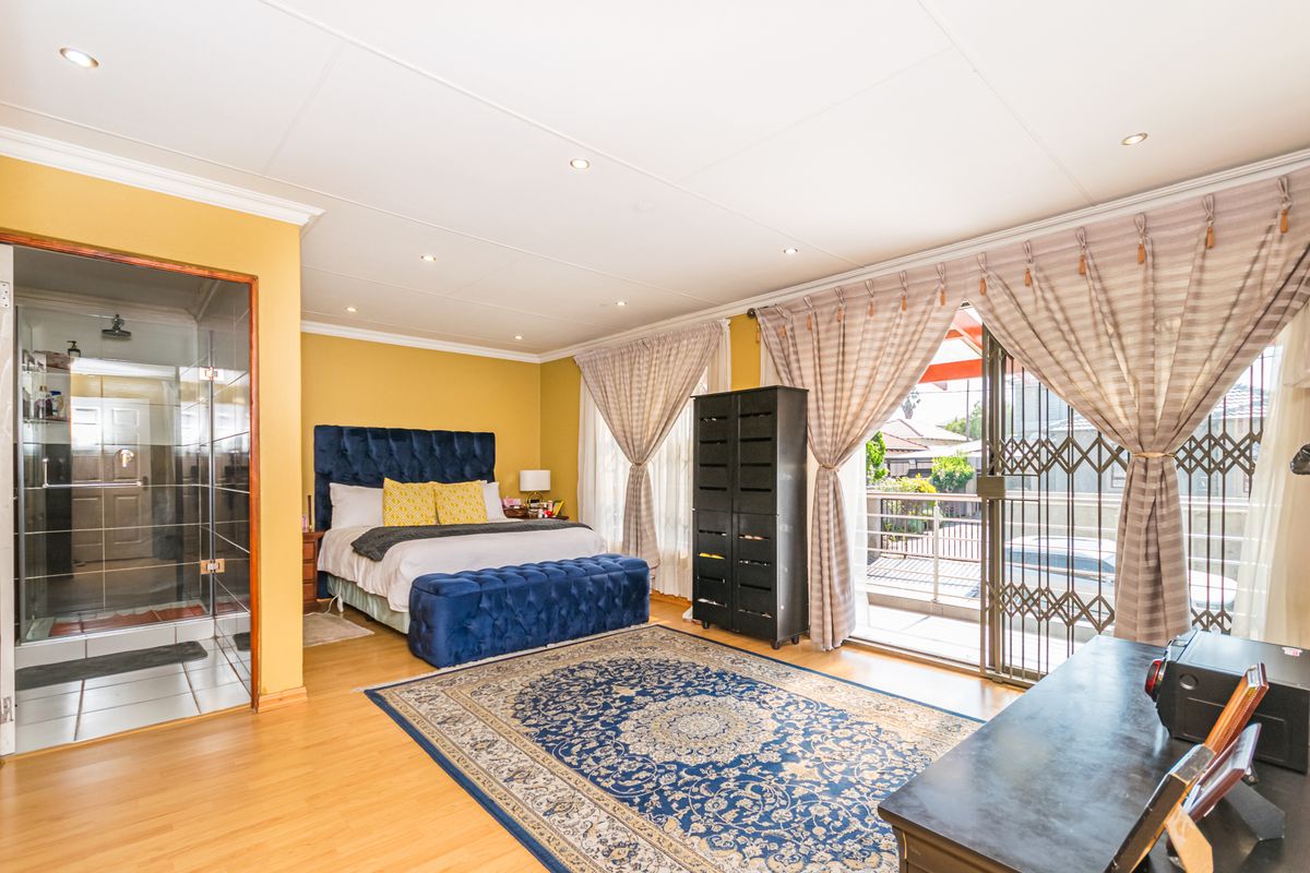 Spacious bedroom featuring laminate flooring, recessed lighting, an en-suite bathroom with a glass shower, and direct access to a private balcony.