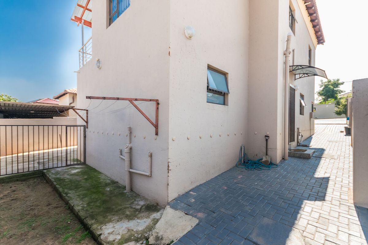 Rear exterior view of the property featuring paved pathways, external plumbing, a security gate, and a wall-mounted clothesline.