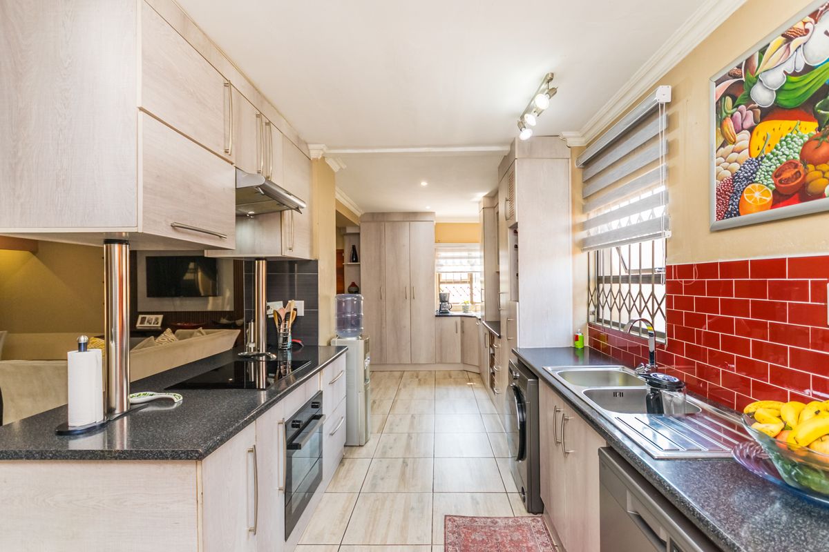 Modern galley-style kitchen featuring light wood cabinetry, dark countertops, red tiled backsplash, integrated appliances, and tiled flooring with ample storage space.