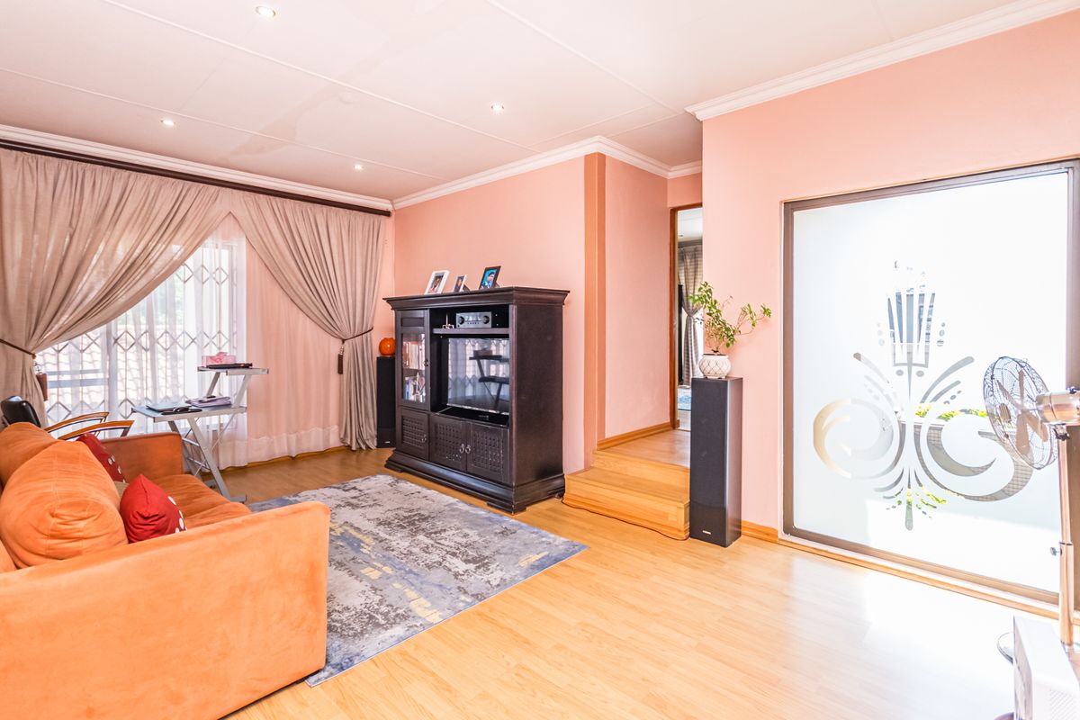 A living room featuring laminate flooring, recessed lighting, and a sliding glass door with a security gate, leading to an adjacent elevated area.