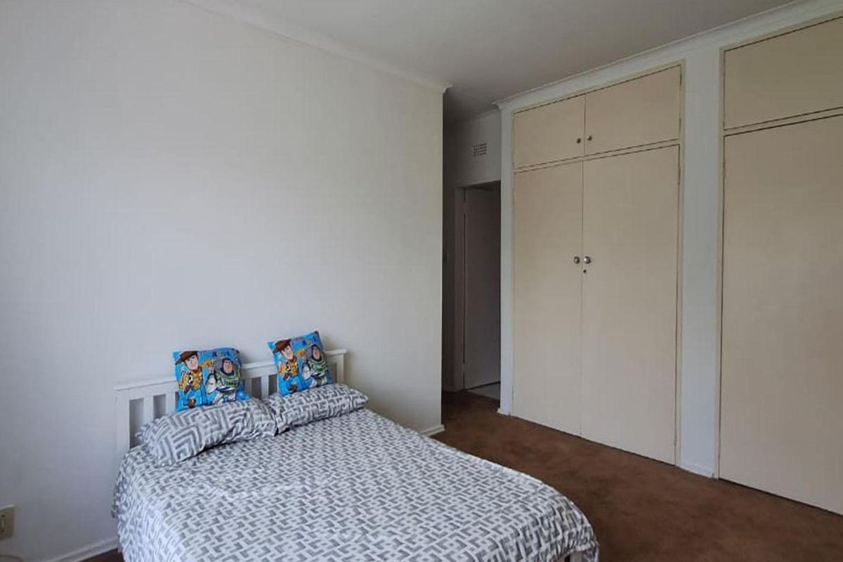 A functional bedroom featuring neutral walls, carpeted flooring, and ample built-in cupboard storage space.
