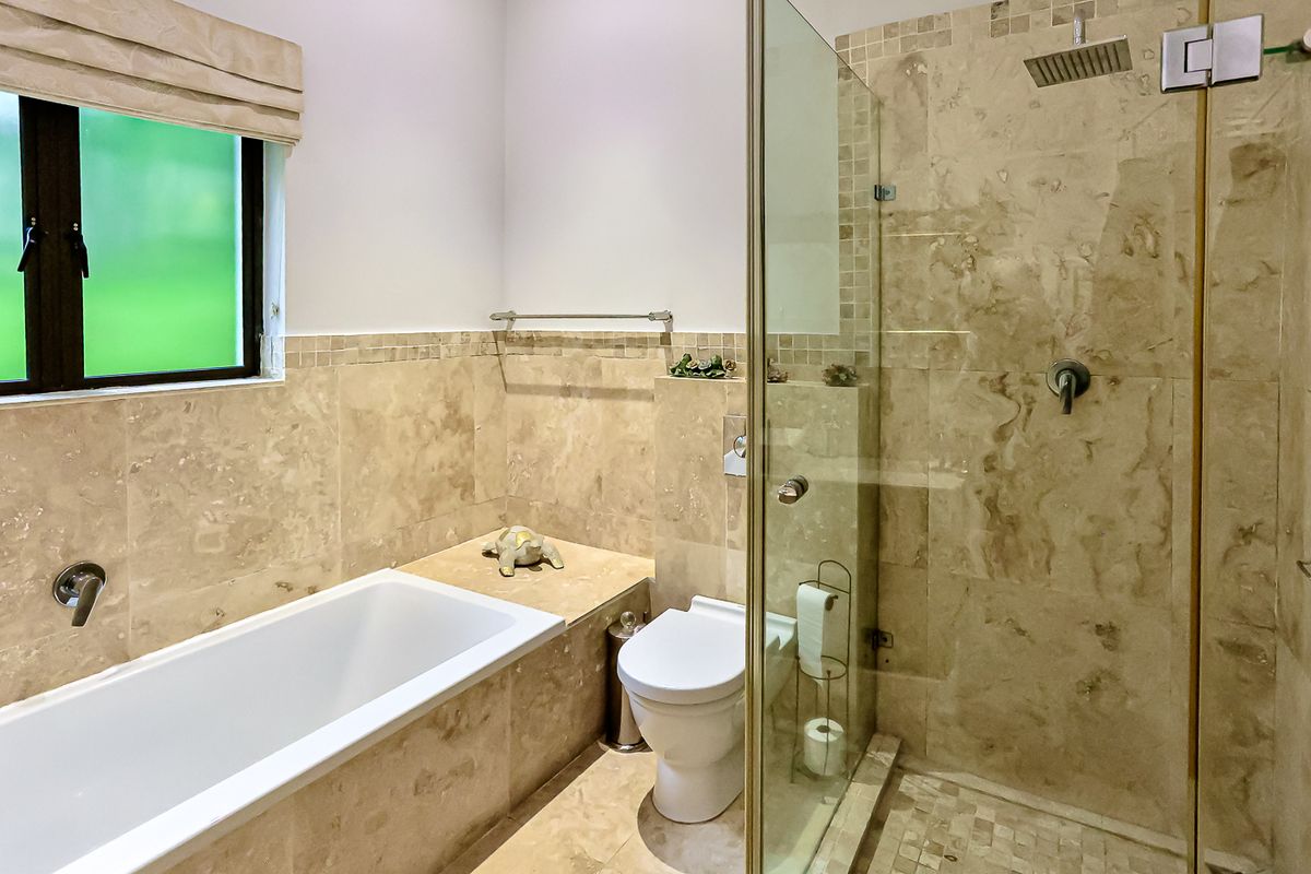 Modern bathroom featuring a built-in bathtub, a separate glass-enclosed shower with a rain shower head, and elegant travertine tiling throughout.