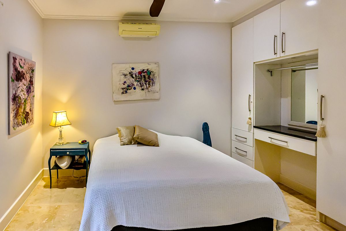 A well-maintained bedroom featuring built-in cupboards, a vanity area, stone flooring, and wall-mounted air conditioning.