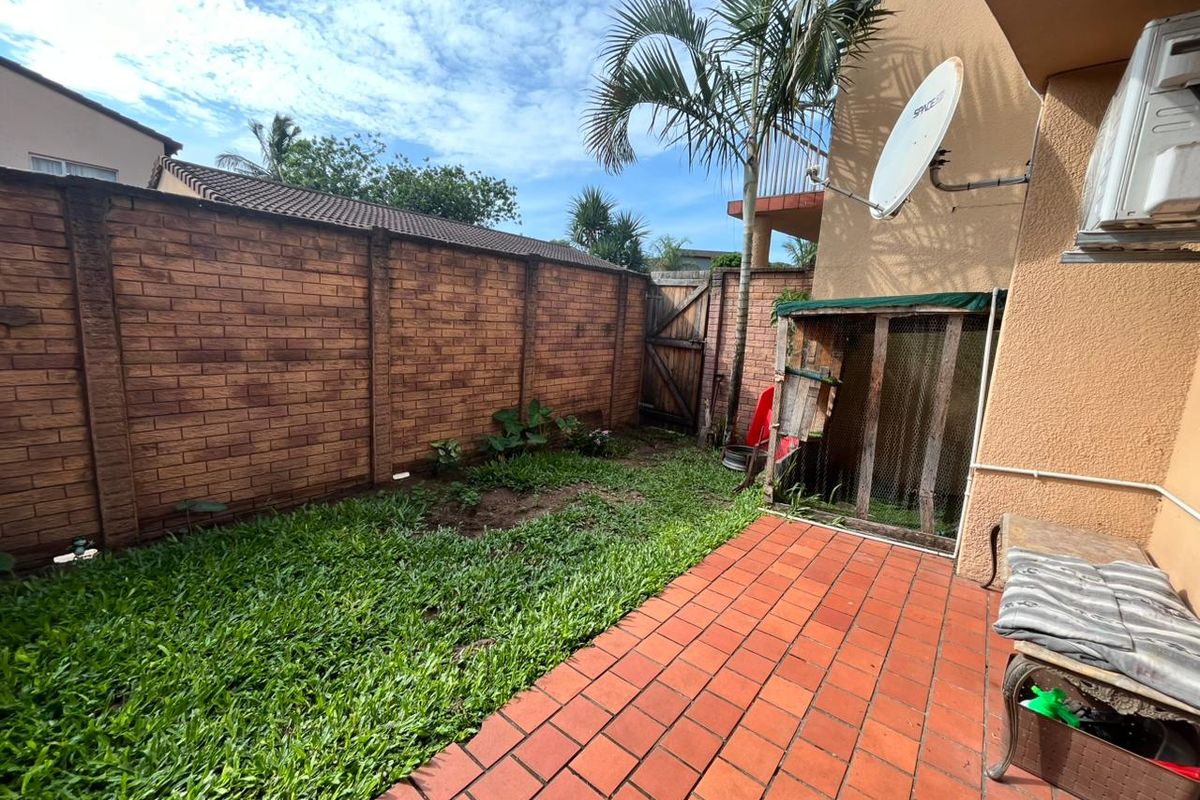 A private rear garden area featuring a paved patio, brick boundary wall, and established lawn space.