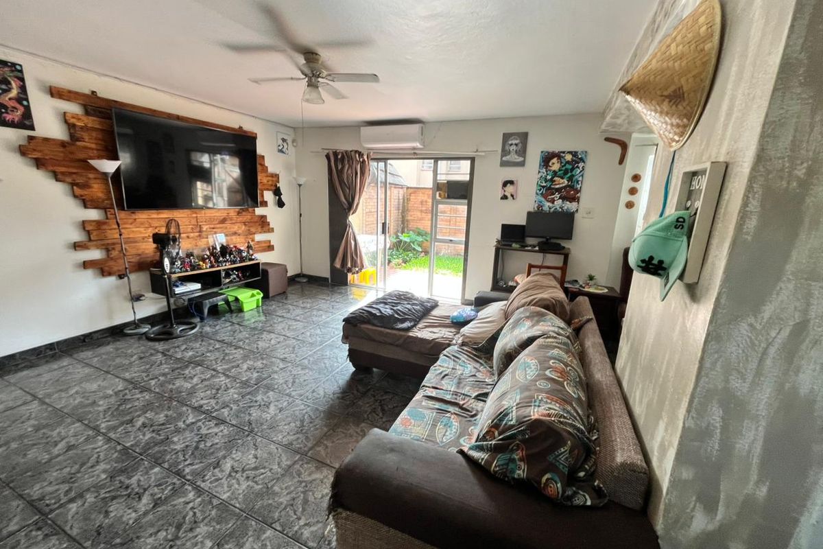 A living room featuring tiled flooring, a ceiling fan, a wall-mounted air conditioning unit, and sliding glass doors providing access to the rear exterior.