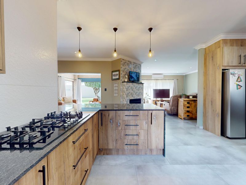 Modern open-plan kitchen featuring wood-finish cabinetry, granite countertops, and a gas hob, flowing seamlessly into the living area with views of the garden.