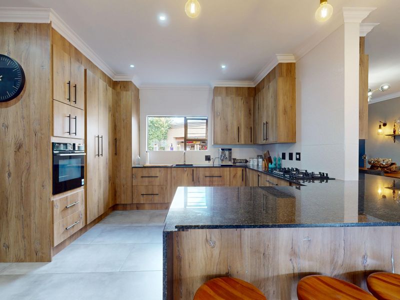 Modern kitchen featuring wood-look cabinetry, granite countertops, built-in oven, and gas hob, offering a functional and stylish workspace.