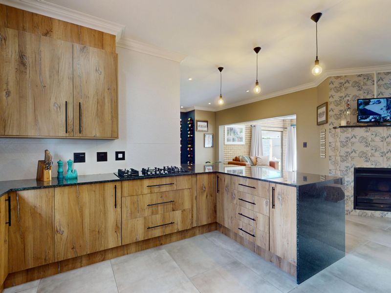 Modern open-plan kitchen featuring wood-grain cabinetry, granite countertops, and a gas hob, seamlessly flowing into a living area with a built-in fireplace.