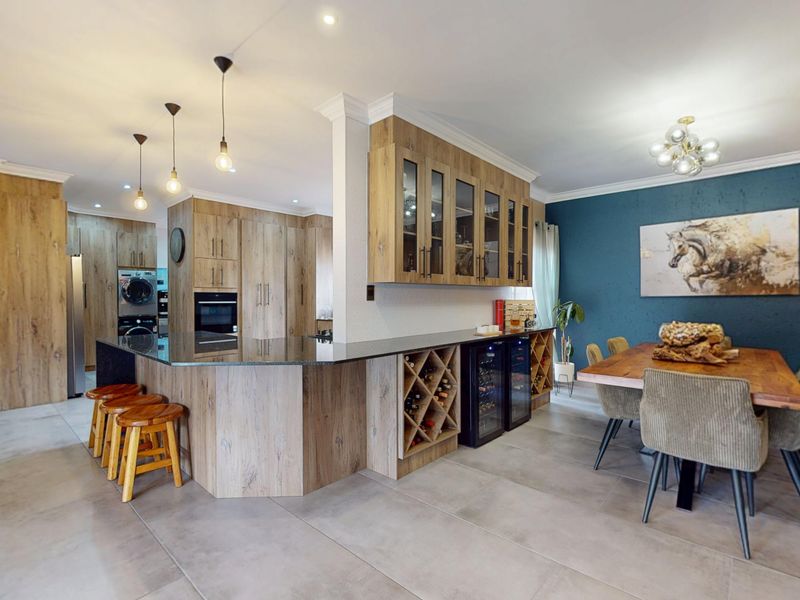 Modern open-plan kitchen and dining area featuring wood-grain cabinetry, stone countertops, integrated wine storage, and sleek tiled flooring.