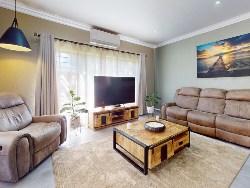 A well-maintained living room featuring tiled flooring, crown molding, recessed downlighting, and a wall-mounted split-system air conditioning unit.