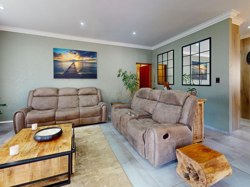 A well-maintained living room featuring neutral green walls, crown molding, recessed lighting, and modern tiled flooring, creating a comfortable and inviting atmosphere.
