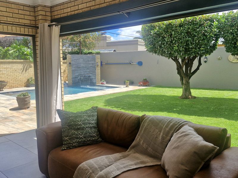 Covered patio area with tiled flooring, seamlessly connecting to a landscaped garden and swimming pool with a built-in water feature.