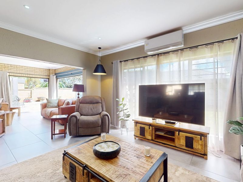 Spacious open-plan living area featuring tiled flooring, recessed downlighting, and a wall-mounted split-system air conditioner, seamlessly connecting to an adjacent patio space.