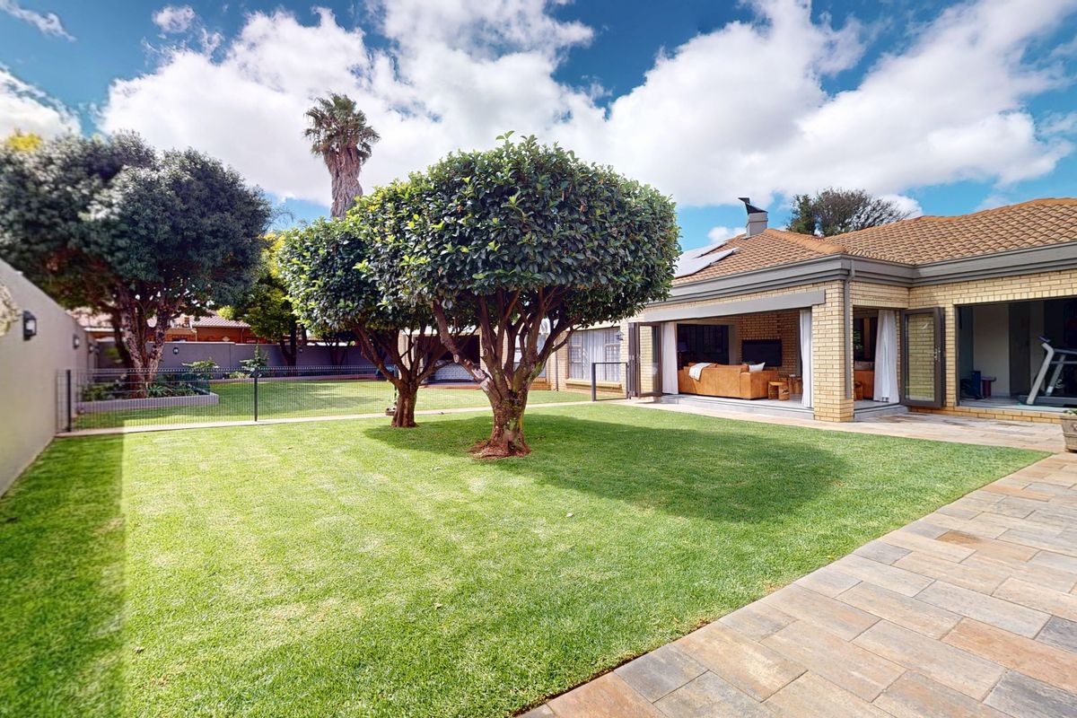 A well-maintained rear garden featuring a paved patio area, lush lawn, and seamless indoor-outdoor flow through large bi-fold doors.