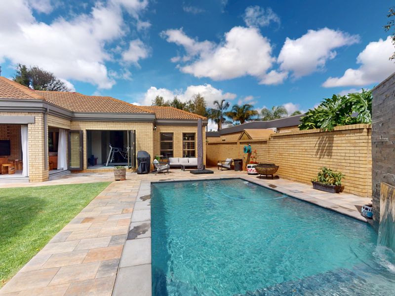 A well-maintained outdoor entertainment area featuring a swimming pool with a stone water feature, paved patio, and a covered terrace.