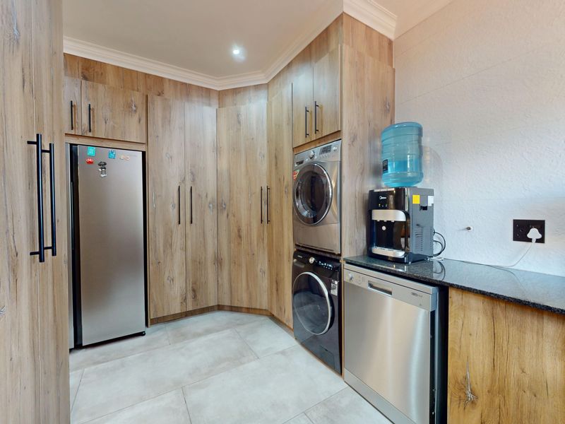 A modern, well-organized laundry room featuring wood-grain built-in cabinetry, stone countertops, and tiled flooring with integrated appliance spaces.