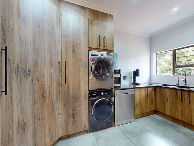 Modern laundry room featuring wood-look cabinetry, stone countertops, an undermount sink, and integrated appliance housing for a sleek, functional workspace.