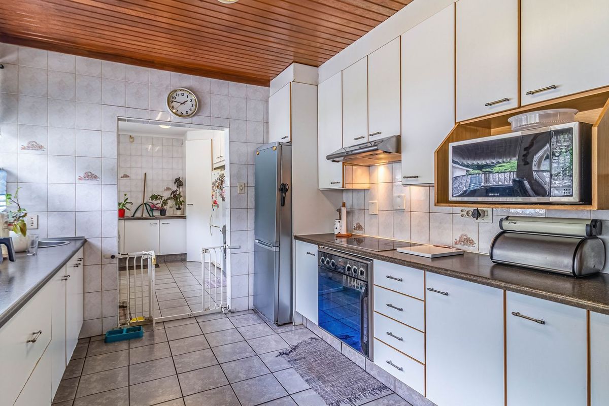 A functional kitchen featuring white cabinetry, laminate countertops, ceramic tile finishes, and a timber ceiling, with an adjoining scullery area.