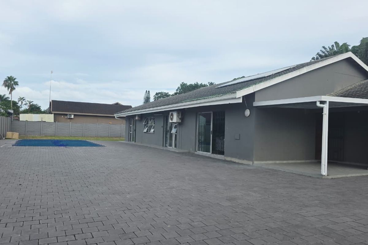 Rear exterior view featuring a large paved area, swimming pool with cover, and a covered carport attached to the main dwelling.