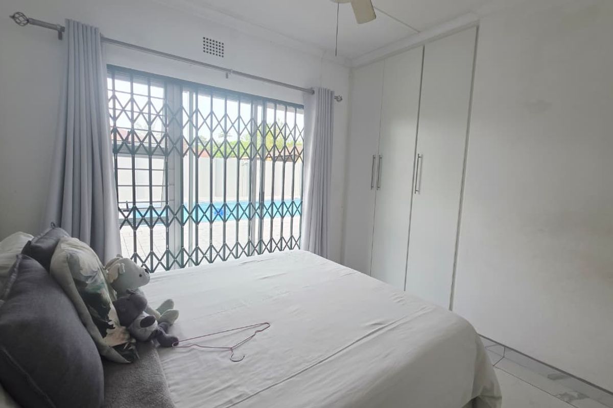 A bedroom featuring built-in cupboards, tiled flooring, and a sliding door with a security gate leading to the pool area.