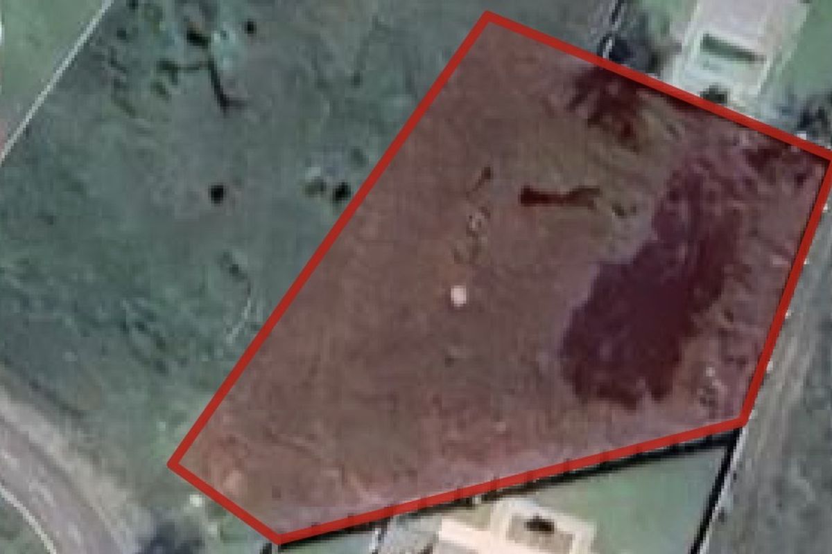 An aerial view of a vacant residential plot outlined in red, showing the land boundaries and surrounding landscape.