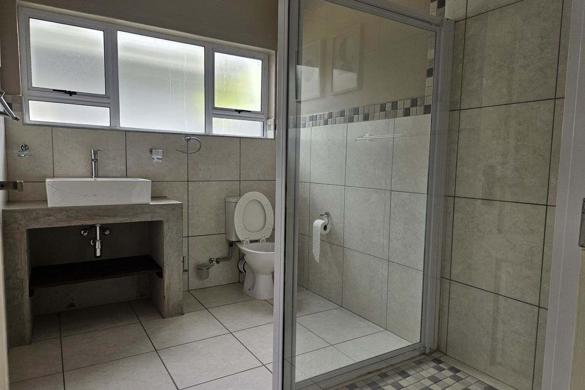 A clean, modern bathroom featuring a concrete vanity with a vessel sink, a glass-enclosed shower, and neutral ceramic tiling throughout.