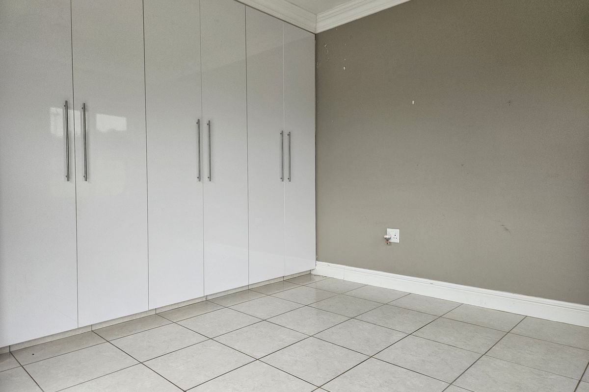 A clean, empty bedroom featuring modern white built-in cupboards, neutral tiled flooring, and crown molding.