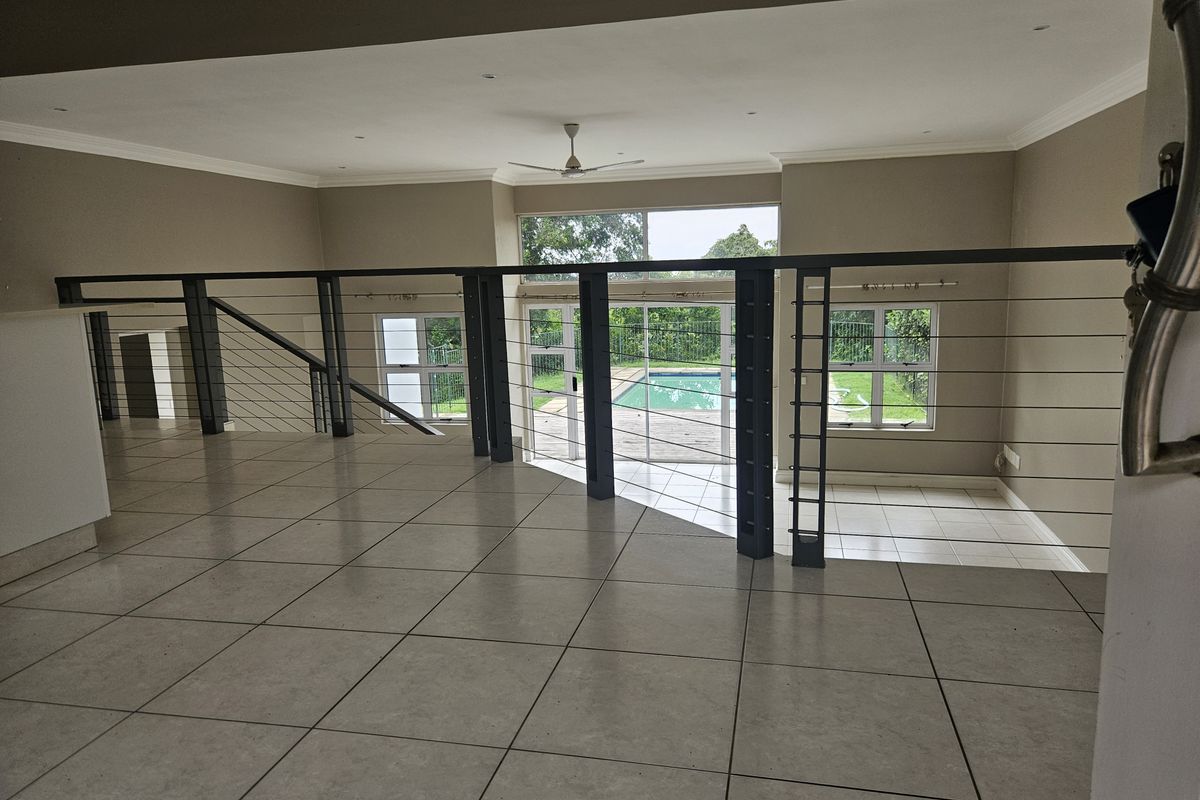 Spacious open-plan living area featuring neutral tiled flooring, a modern metal balustrade, and large sliding doors overlooking the swimming pool and garden.