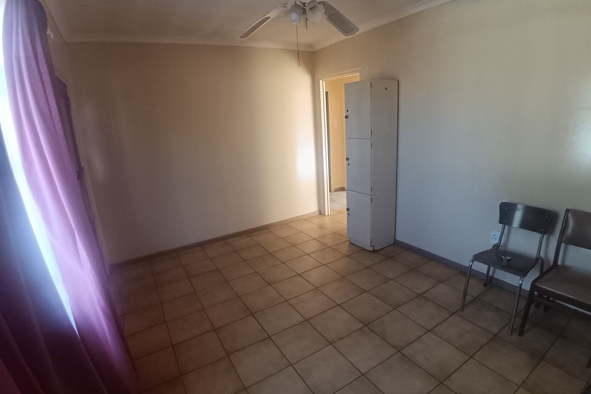 A simple bedroom featuring tiled flooring, a ceiling fan, and a built-in storage unit.