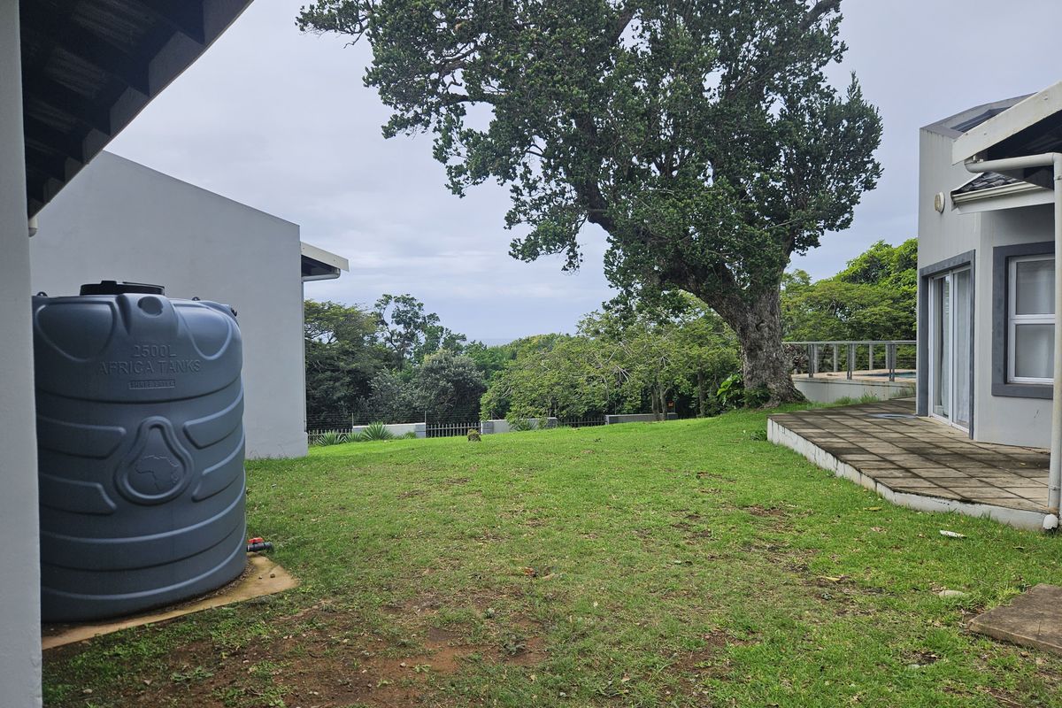 Rear garden area featuring a lawn, paved patio section, and a large water storage tank with mature trees in the background.