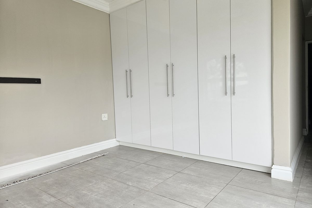 A clean, empty bedroom featuring modern white built-in cupboards, neutral wall tones, and grey tiled flooring.