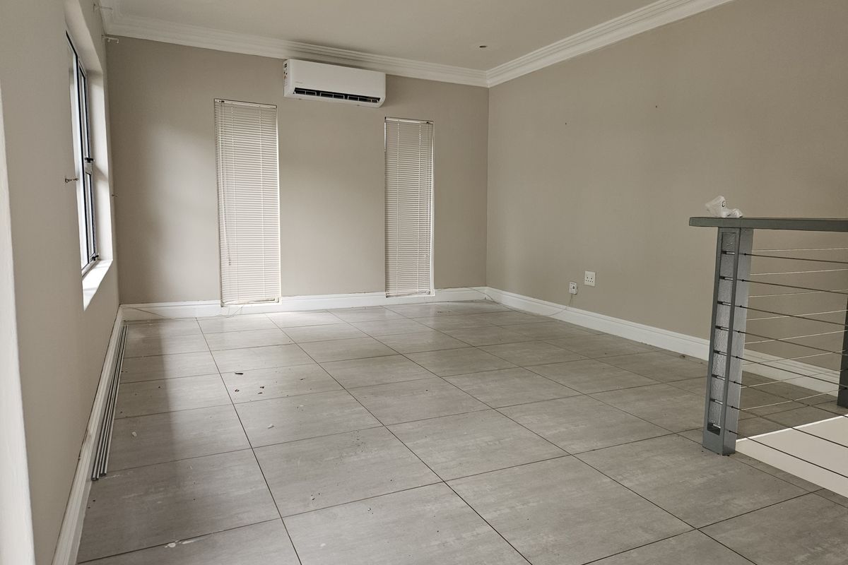 An empty, open-plan living area featuring neutral tiled flooring, a wall-mounted air conditioning unit, and a modern metal balustrade.
