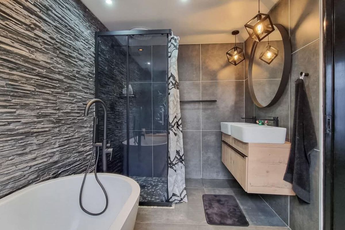 Modern bathroom featuring a freestanding bathtub, walk-in shower, wall-mounted double vanity, and striking stone feature wall with contemporary lighting.