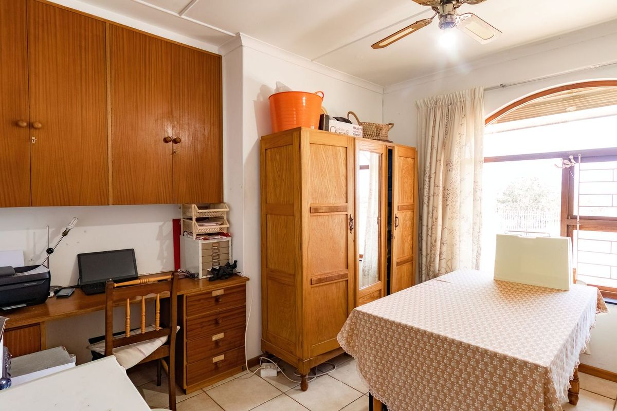 A functional bedroom or study space featuring built-in wooden cabinetry, tiled flooring, and an arched window providing natural light.