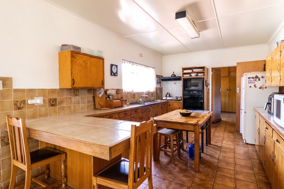A functional kitchen featuring wooden cabinetry, tiled countertops, a built-in oven, and a breakfast bar area with tiled flooring.