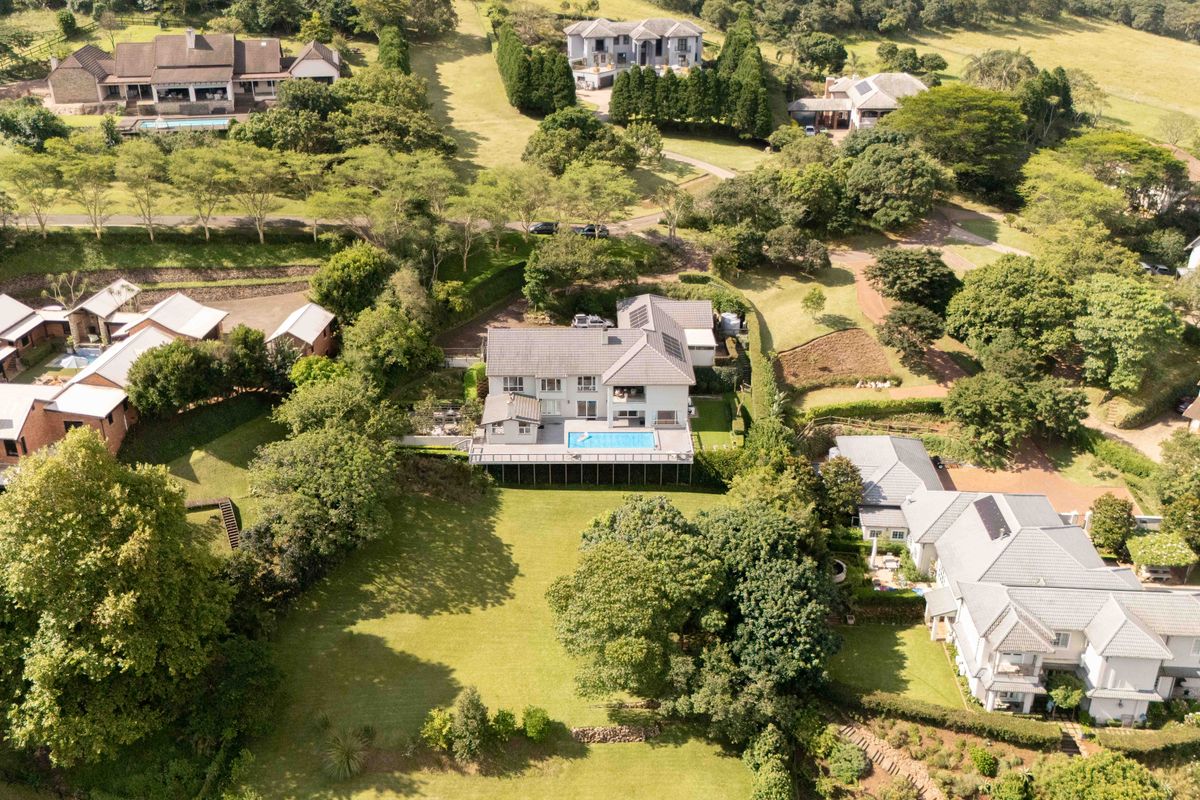 Aerial view of a residential townhouse property featuring a private swimming pool, expansive lawn, and elevated deck within a landscaped estate setting.