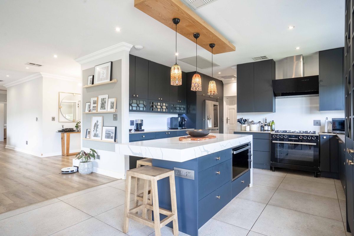 Modern open-plan kitchen featuring dark cabinetry, a central island with stone countertop, integrated oven, and stylish pendant lighting.
