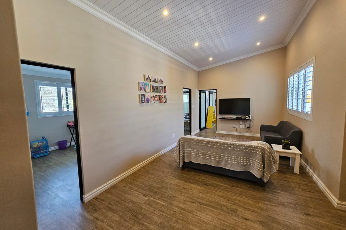 A spacious living room featuring wood-look flooring, a vaulted tongue-and-groove ceiling with recessed lighting, and plantation shutters on the windows.