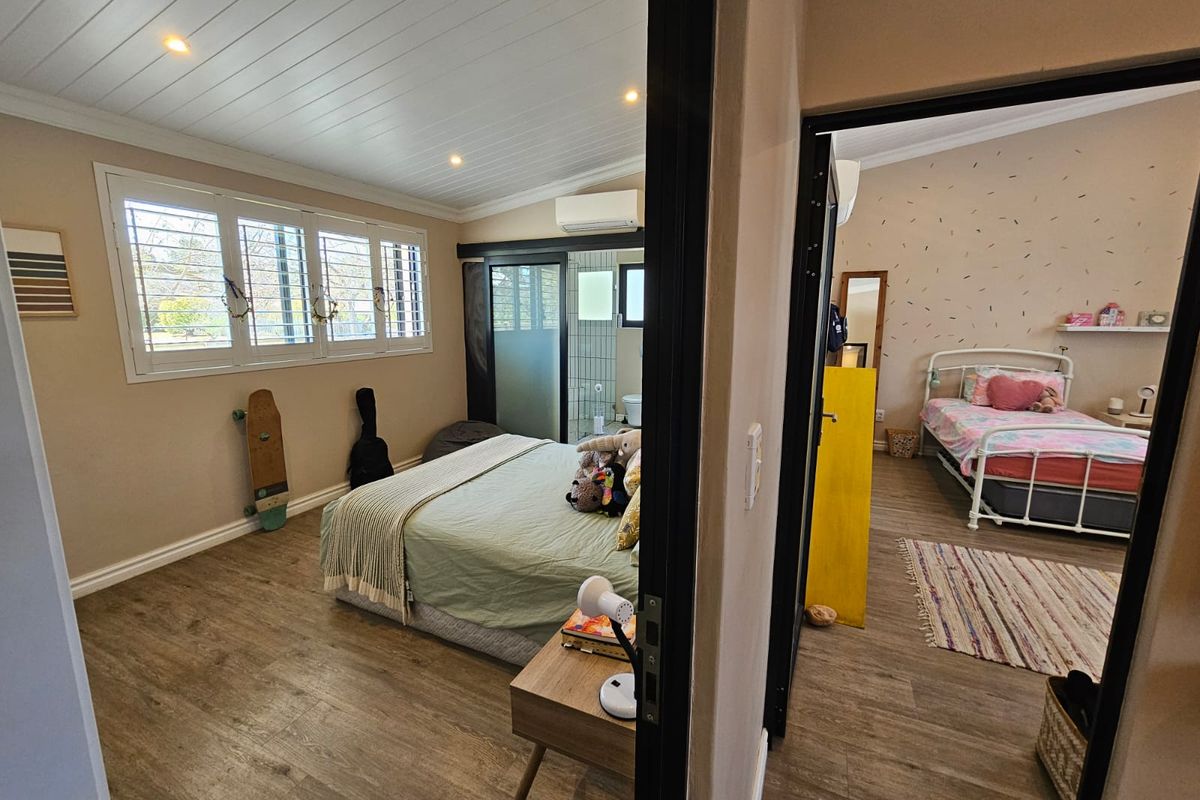 A view through a doorway into a bedroom featuring wood-look flooring, plantation shutters, and an en-suite bathroom with a sliding door.