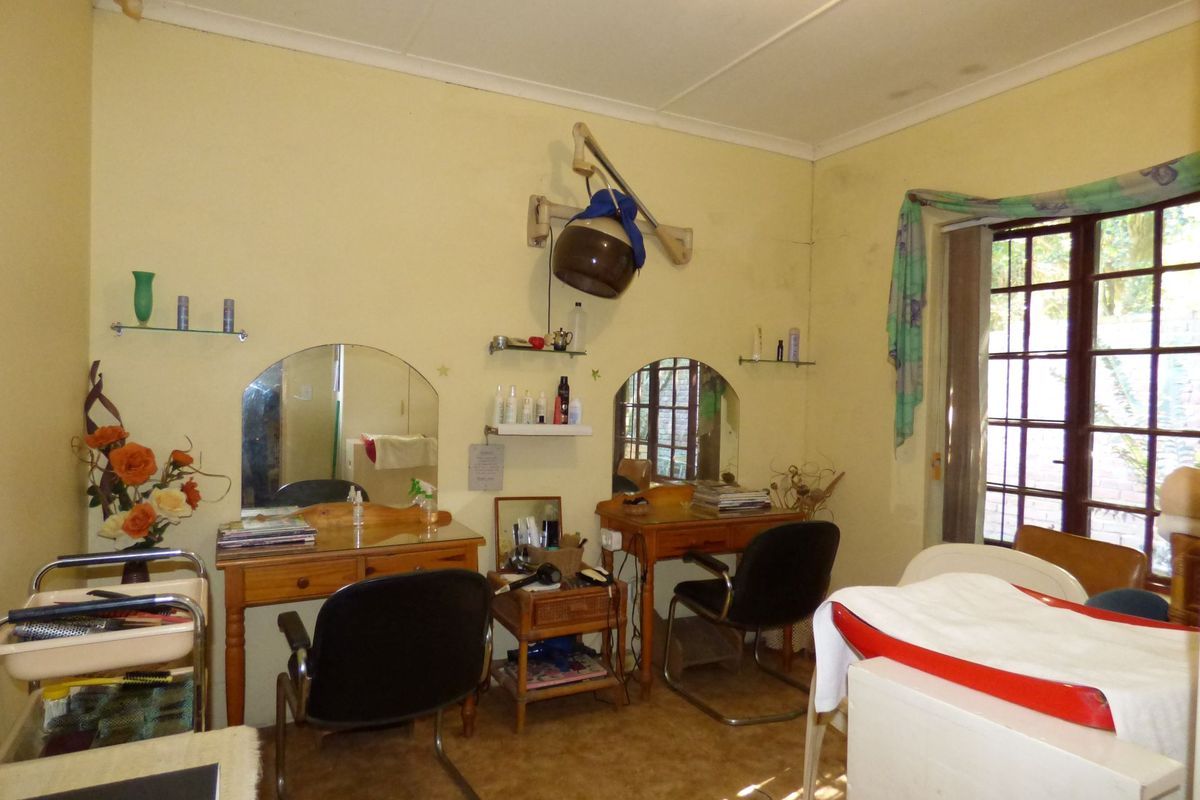 A bedroom space currently utilized as a salon, featuring timber-framed windows and coved cornicing, requiring cosmetic updates to the walls and flooring.