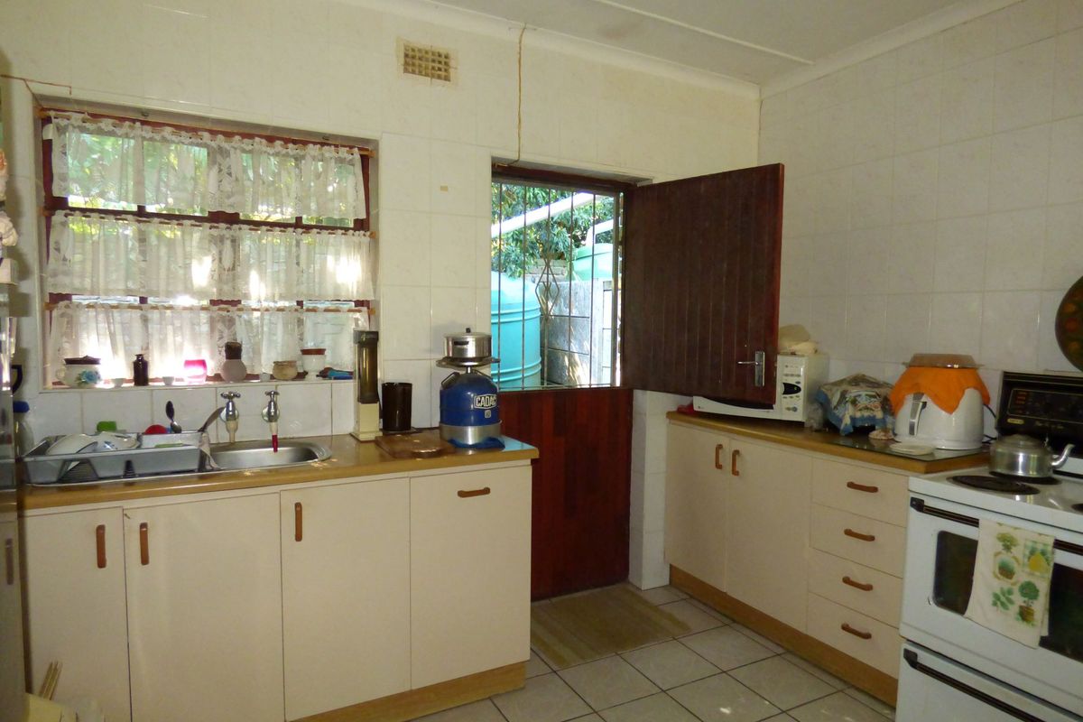 A functional kitchen featuring tiled splashbacks, built-in cabinetry, a stainless steel sink, and a freestanding oven with direct access to the exterior.