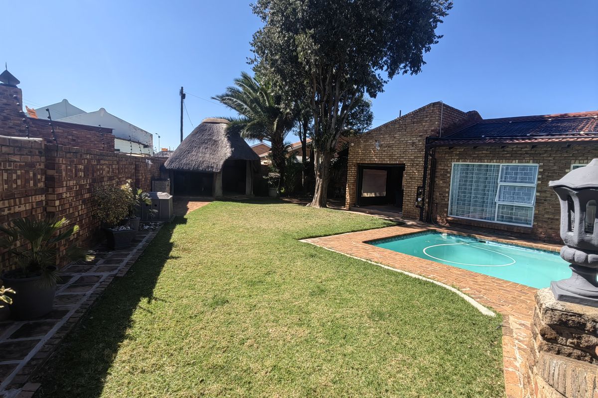 Spacious rear garden featuring a swimming pool with solar heating, a traditional thatched lapa, and established brick boundary walls.