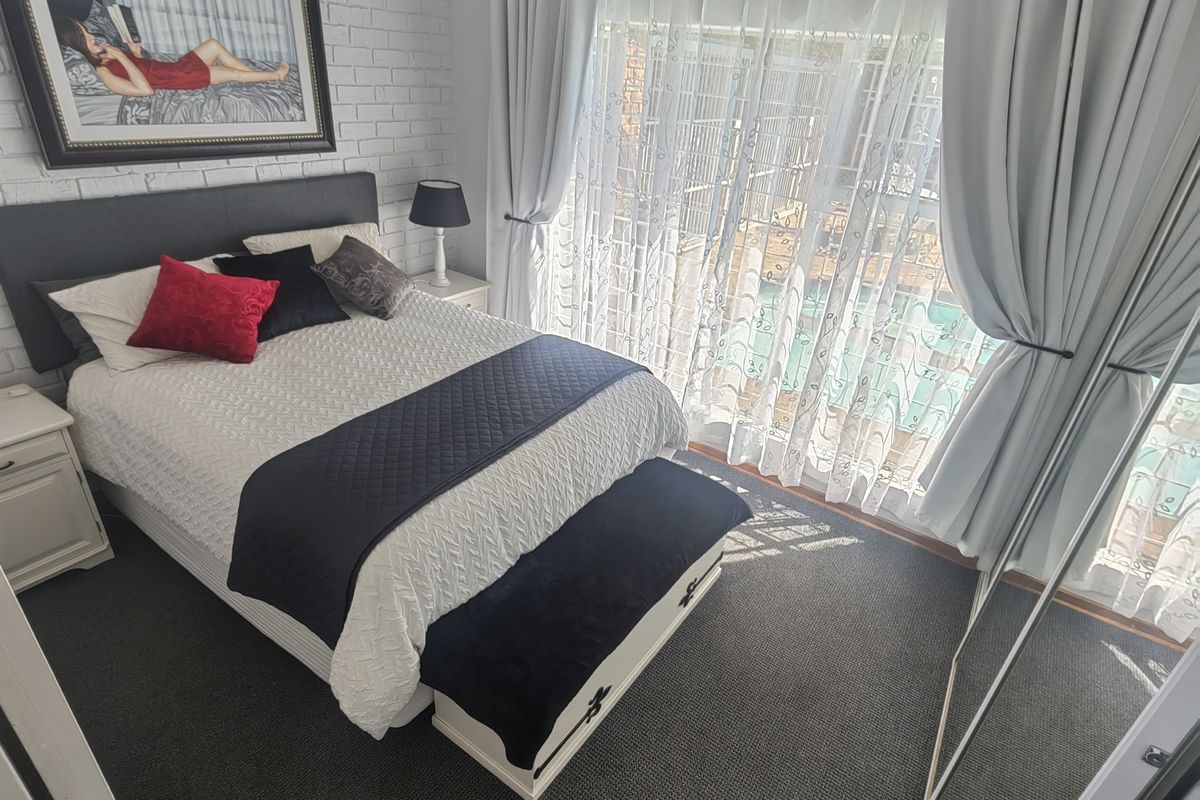A well-maintained bedroom featuring a painted brick feature wall, carpeted flooring, and a large sliding glass door providing access to the outdoor area.