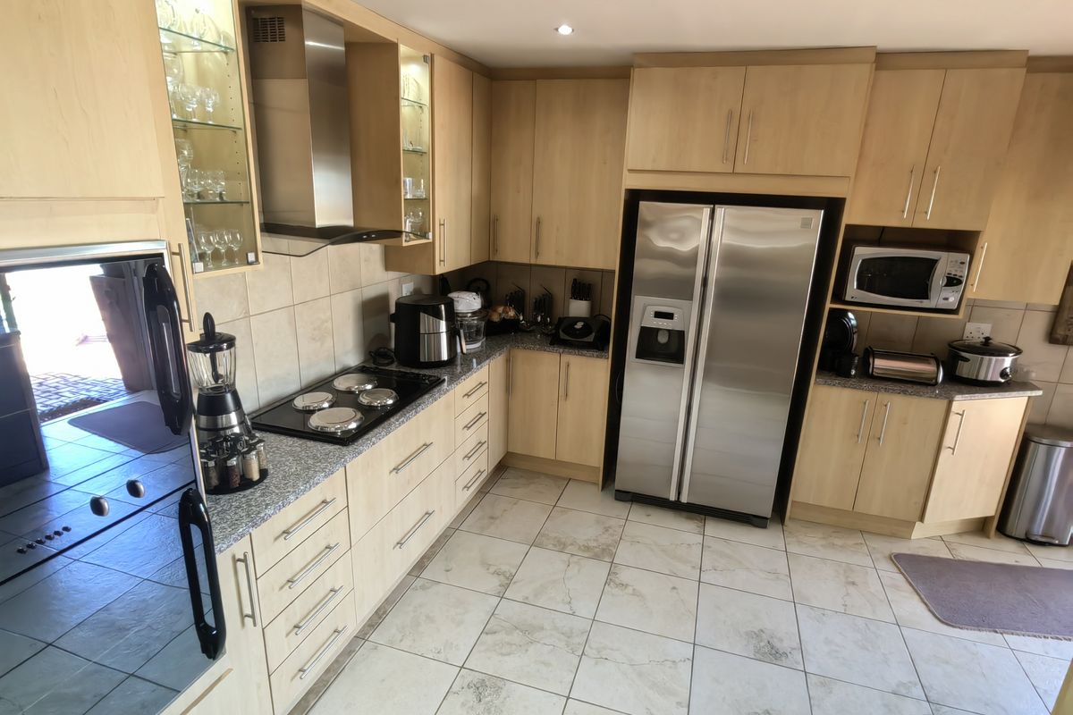 A functional kitchen featuring light wood cabinetry, granite countertops, integrated stainless steel appliances, and tiled flooring with ample storage space.